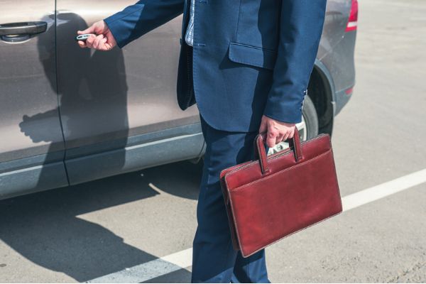 Agente di commercio in giacca con la borsa da lavoro apre la sua auto a noleggio lungo termine